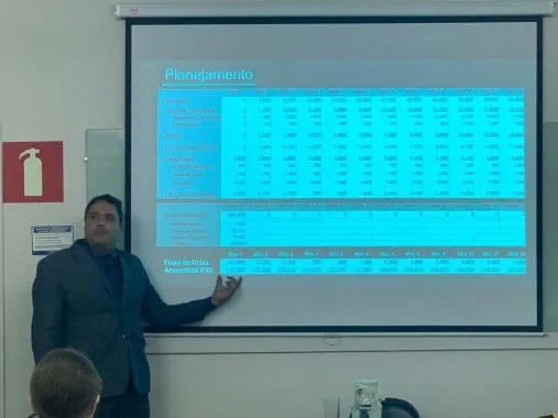 Edilson Junior, CEO da CF Contabilidade, ministra palestra no Big Shopping. Ele aponta uma projeção repleta de números em uma planilha intitulada “Planejamento”