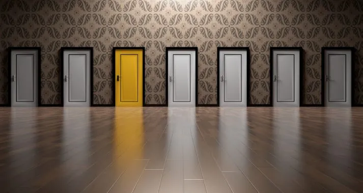 Uma série de portas enfileiradas se apresenta ao longo de uma parede com estampa. A terceira porta da esquerda para a direita está marcada com cor diferente. Ela representa uma decisão mais assertiva que o gestor pode tomar partindo dos dados em uma DRE.