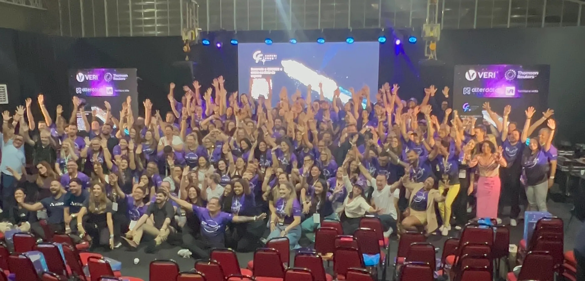 Franqueados e time da CF reunidos no palco da CF Tech, 9ª convenção da rede, com os braços para cima e camisas roxas do evento